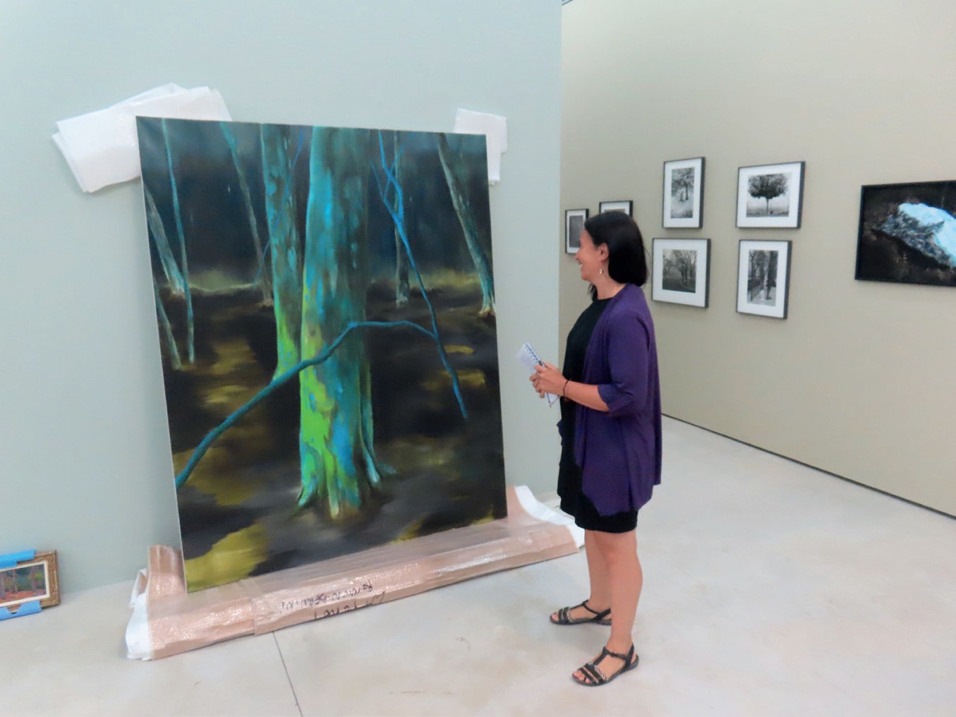 Une femme se tient à côté d'une grande peinture représentant une forêt