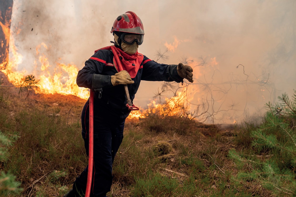 Un pompier en tenue de feu devant un incendie de forêt